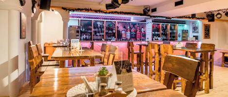 A restaurant with wooden tables and chairs, a bar area with bottles, and a sign for 'STIRIA'.