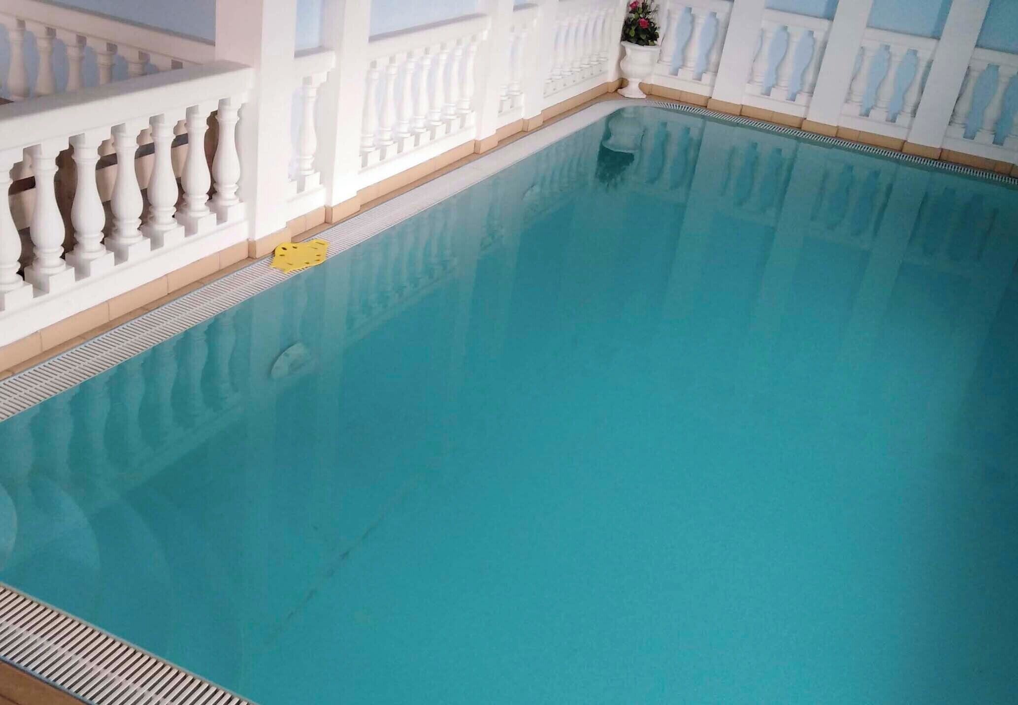 Ein großes Hallenbad mit einer gefliesten Liegefläche und einem weißen Geländer.