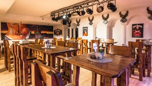 A restaurant interior with wooden tables and chairs, a ceiling-mounted lighting system, and wall decorations including posters and animal horns. - Hotel Styria (Chvalovice)