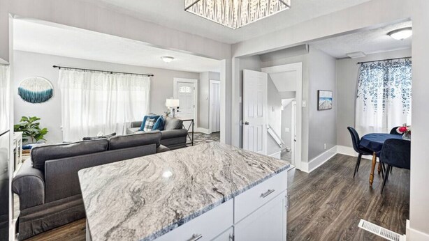 Een moderne woonkamer met een marmeren eiland, een grijze bank en een eethoek met een tafel en stoelen.