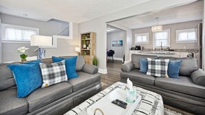 Een moderne woonkamer met twee grijze banken, een salontafel en een keuken op de achtergrond.