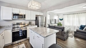 Een moderne keuken met witte kastjes, roestvrijstalen apparatuur en een marmeren aanrecht.