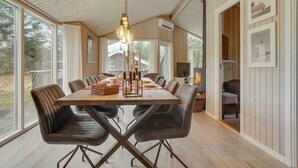Un espace repas avec une table et des chaises en bois, de grandes fenêtres et un luminaire suspendu.