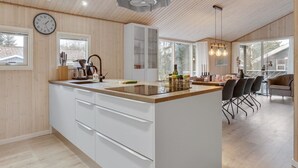 Une cuisine moderne dotée d’un grand îlot central, de meubles blancs et d’un plafond en bois.