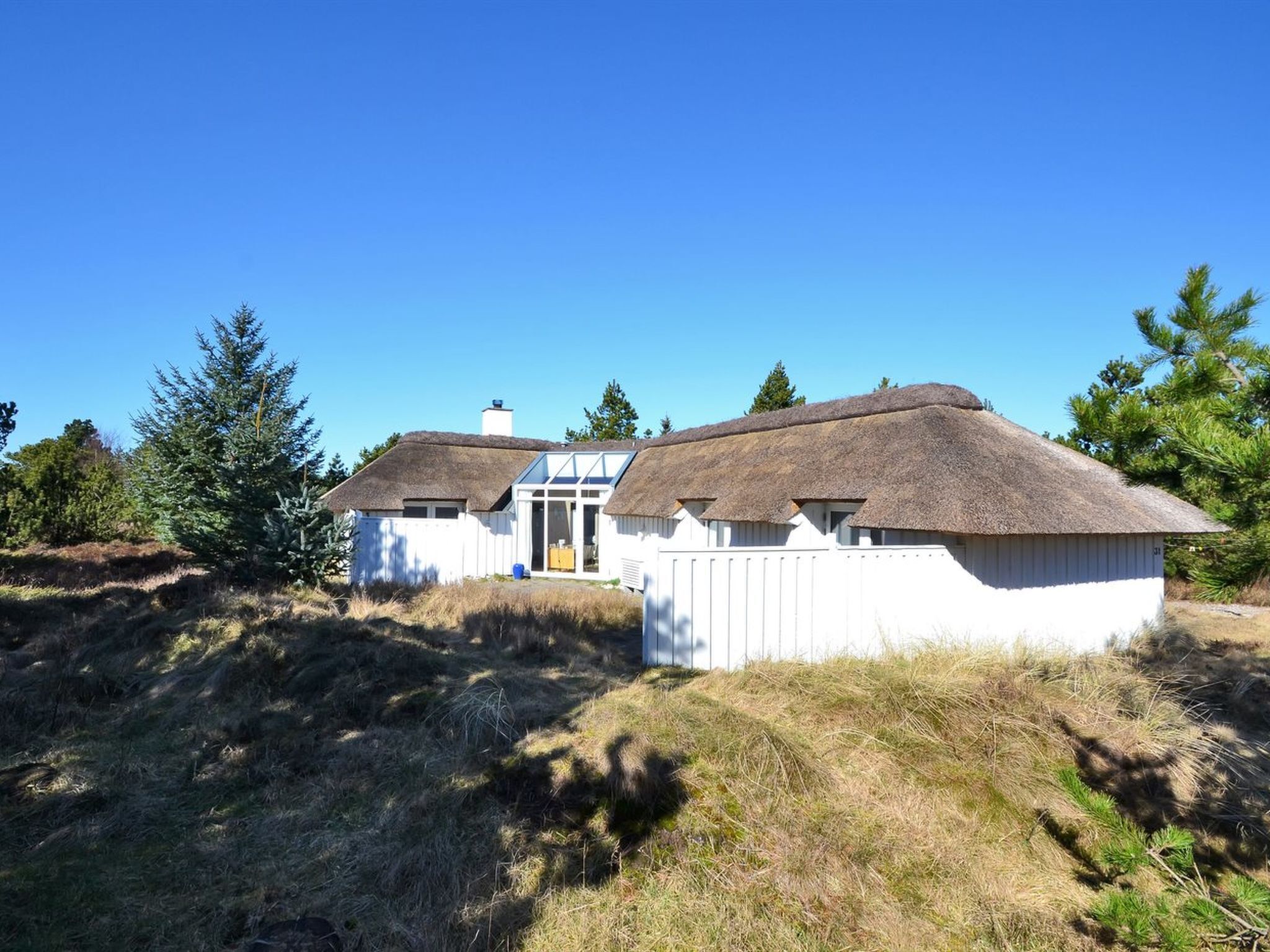 A white cabin with a thatched roof, surrounded by trees and grass.
