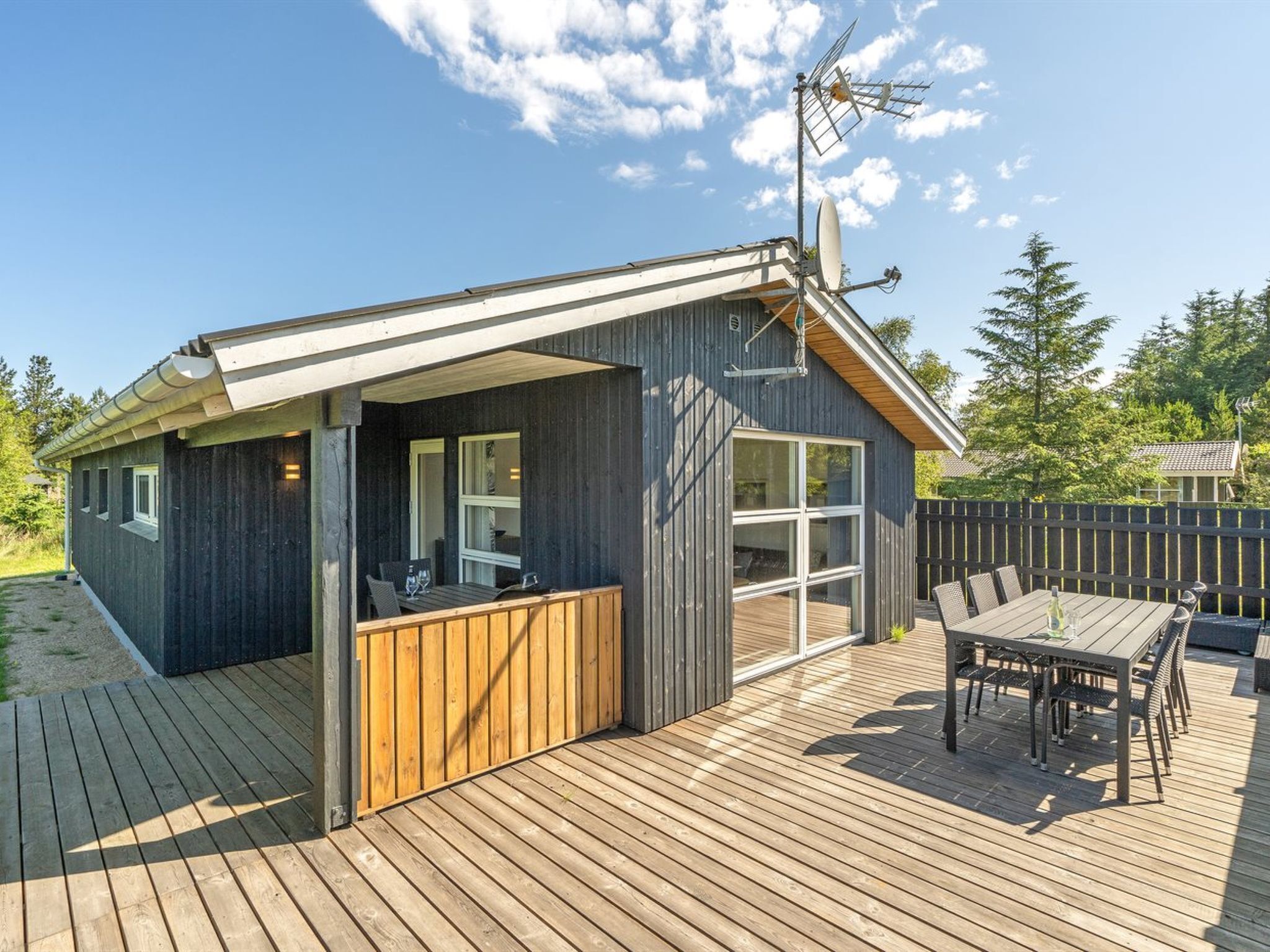 Une cabane moderne dotée d’une terrasse, de grandes fenêtres et d’une antenne parabolique.