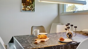 Un comedor con una mesa dispuesta para dos, con mantel negro decorado con dibujos blancos, un croissant, un muffin, una taza y una taza de café.