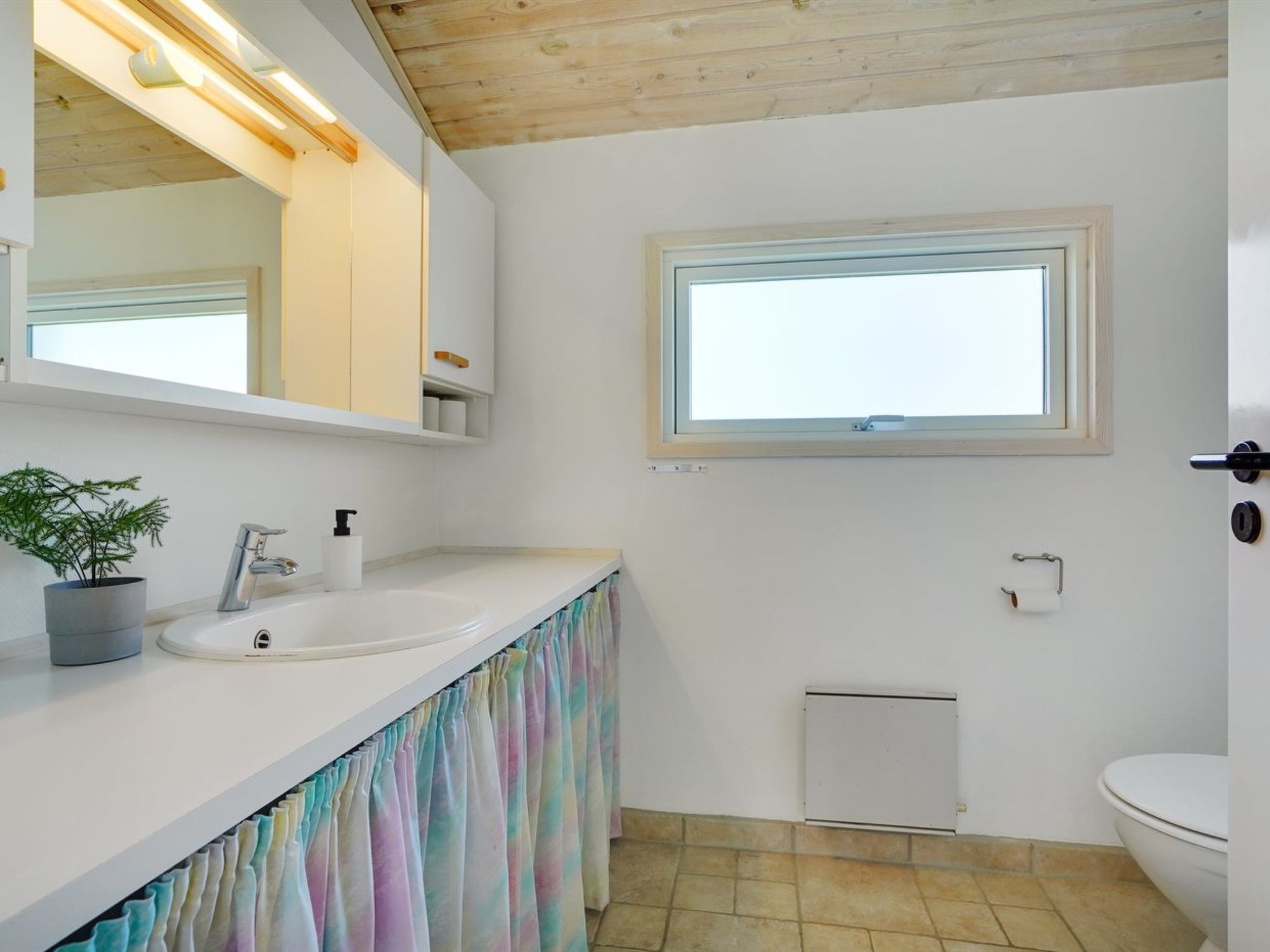 A bathroom with a white sink, a mirror, a window, and a toilet.
