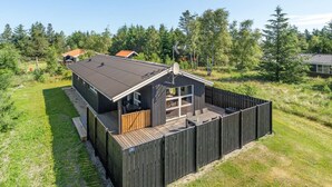 Una cabaña moderna con terraza, rodeada por una valla de madera y un césped.