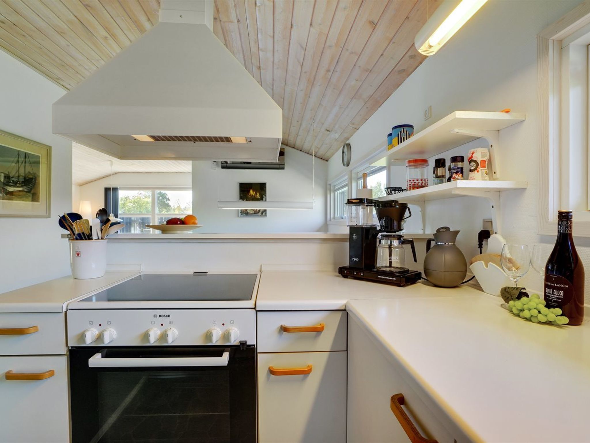 A modern kitchen with white cabinetry, a Bosch oven, a coffee maker, and a wine bottle on the counter.