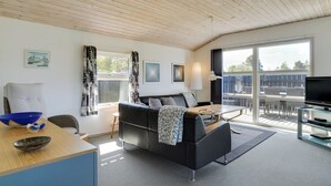 Una sala de estar moderna con un sofá negro, techo de madera y un ventanal con vistas al exterior.