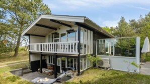 Ein zweistöckiges Haus mit einem Balkon, einer Terrasse mit Tisch und Stühlen und einem großen Fenster.