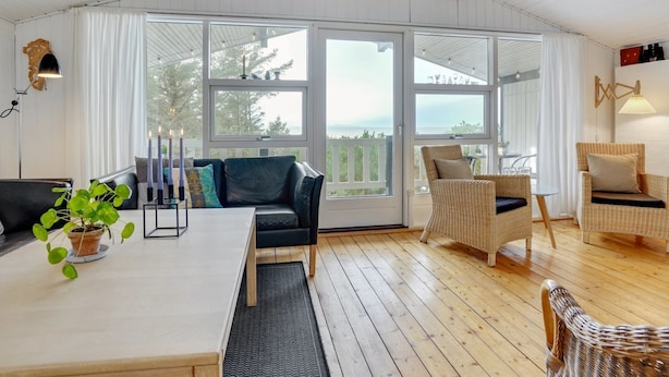 Ein gemütliches Zimmer mit Holzboden, einem schwarzen Ledersofa, Korbstühlen und einem Tisch mit Kerzen.