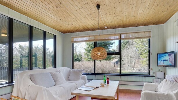 A modern living room with a white sofa, a wooden coffee table, and large windows offering a view of the outdoors.