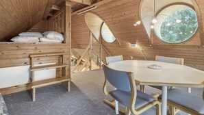 Ein gemütliches Holzinterieur mit einem runden Esstisch, Bänken und einem Schlafstock mit Kissen.