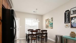 A dining area with a wooden table and chairs, a black refrigerator, a trash can, and a welcome sign on the wall.