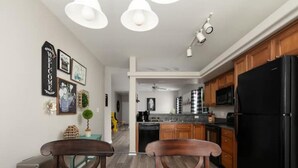 A modern kitchen with wooden cabinets, a black refrigerator, and a dining area with two chairs and a table.