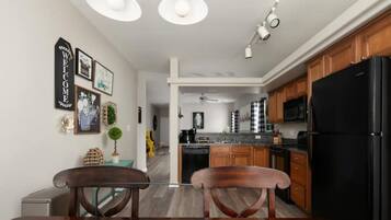 A modern kitchen with wooden cabinets, a black refrigerator, and a dining area with two chairs and a table.