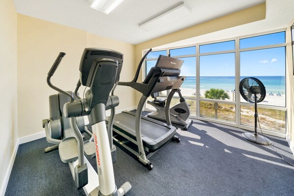 A gym with cardio equipment and a view of the beach.
