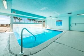 An indoor swimming pool with a clear blue water, a metal pool ladder, and a sign indicating no diving or jumping.