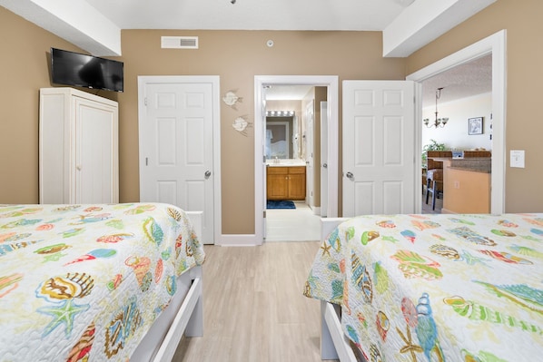 A bedroom with two beds, a television, and a bathroom visible through an open door.