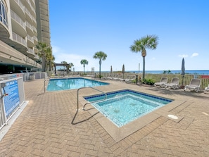 A pool area with two rectangular pools, lounge chairs, and a view of the ocean.