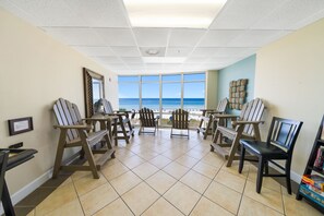 A room with a view of the ocean, furnished with wooden chairs and tables, and a tiled floor.