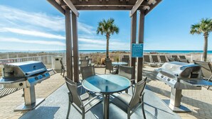Eine Terrassensitzgelegenheit im Freien mit zwei Grillanlagen, einem Tisch mit Stühlen und Blick auf den Strand.