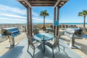 An outdoor patio with two barbecue grills, a table with chairs, and a view of the beach. - Salty Sundaze Beachfront King Master 2 Bed 2 Bath Sleeps 6+ Beach Service (Panama City Beach)
