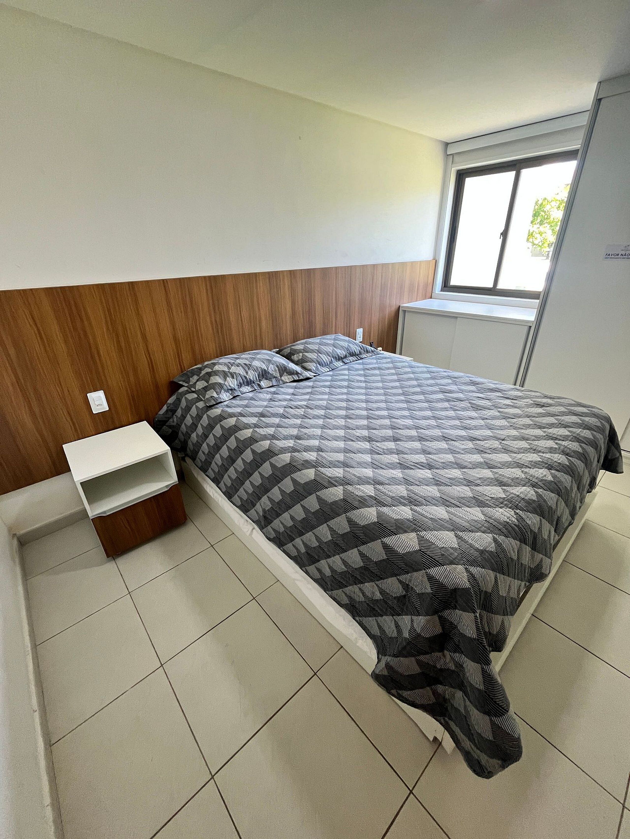 Un dormitorio con cama, mesita de noche, ventana y armario.