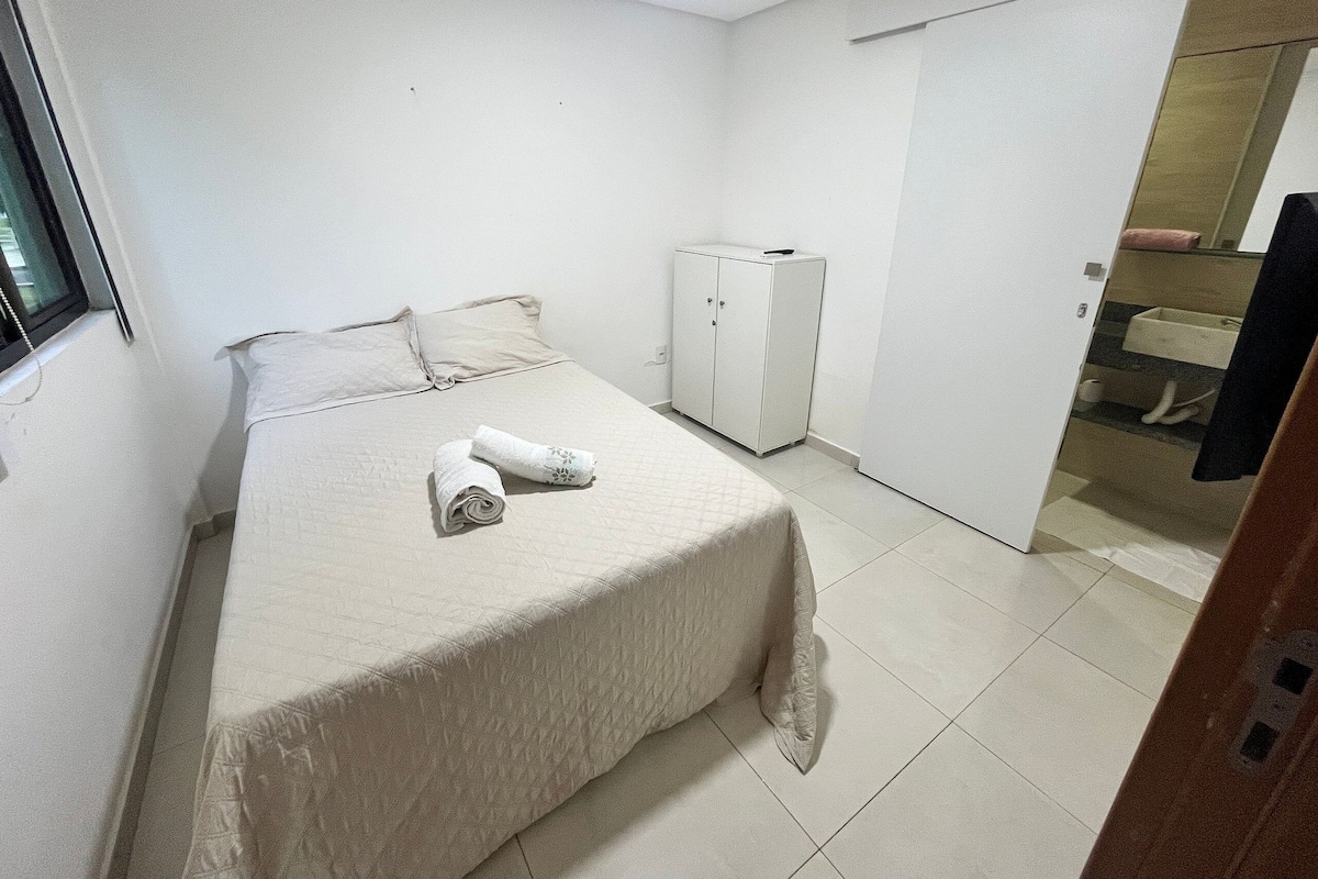Une petite pièce propre, avec un lit, une armoire et une salle de bain visible à travers une porte ouverte.