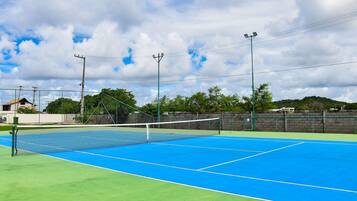 Una cancha de tenis al aire libre con una red, rodeada por una cerca verde y un muro de ladrillo.