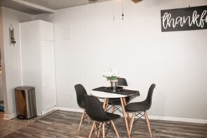 Cozy dining area with a round table and four chairs, a potted plant, and a thoughtful sign.