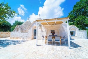 Un bâtiment en pierre doté d’un patio couvert, d’une table et de chaises.
