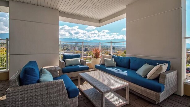 Ein überdachter Außenbereich mit Korbmöbeln und einem blauen Sofa mit Blick auf eine Stadtlandschaft.