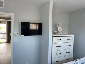 Een slaapkamer met een aan de muur bevestigde televisie, een witte dressoir met lades, en een decoratief beeldje erboven.