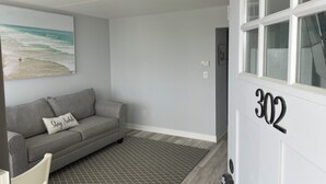 A modern living room with a grey sofa, a framed beach painting, and a number '302' on the wall. - Settle In the Sun!
Fantastic centrally located North Wildwood Condo  (North Wildwood)