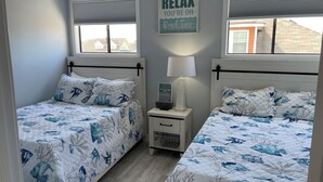 A bedroom with two beds, each with a blue and white aquatic-themed bedspread. There is a nightstand with a lamp and a framed picture between the beds. A sign on the wall reads "RELAX YOU'RE ON BEACH TIME". - Settle In the Sun!
Fantastic centrally located North Wildwood Condo  (North Wildwood)