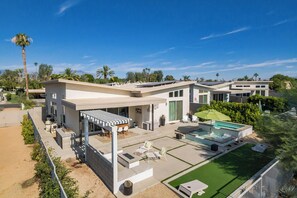A modern house with a patio, outdoor seating, a swimming pool, and a well-maintained lawn.