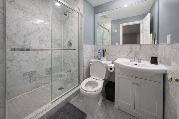 Une salle de bain moderne avec une douche à parois de verre, des toilettes blanches et un lavabo avec un miroir au-dessus.