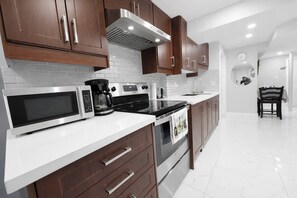 A modern kitchen with stainless steel appliances, wooden cabinets, and a white tiled backsplash. - Modern Cozy Luxury Suite in Ajax | 5 Min to Hwy 401 | Kitchen/ Laundry/Parking  (Ajax)