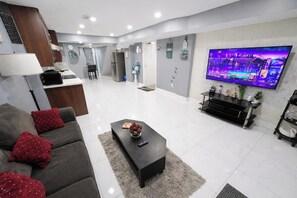 A modern living room with a grey sofa, a coffee table, a flat-screen TV, and a kitchen area in the background. - Modern Cozy Luxury Suite in Ajax | 5 Min to Hwy 401 | Kitchen/ Laundry/Parking  (Ajax)