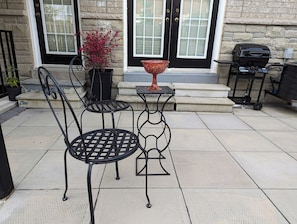 Un patio con dos mesas y sillas de metal, un cuenco rojo y una parrilla de barbacoa.
