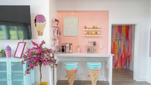 Eine Küche mit rosa Ziegelrückwand, Eiswaffel-Hocker und einem Schild, das Eissorten auflistet.