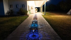 Ein Weg führt zu einem Gebäude mit überdachter Veranda, einem kleinen Garten und einem Zelt auf der Wiese.