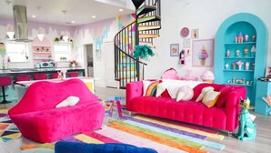 Ein helles Wohnzimmer mit einem rosafarbenen Sofa, einem blauen Sessel und einem farbenfrohen Teppich.