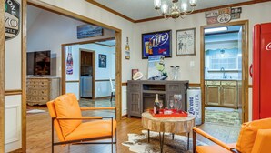 Een woonkamer met oranje fauteuils, een ronde houten salontafel en een koelkast.