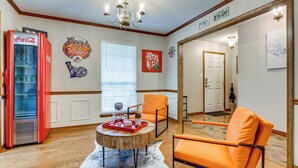 Een woonkamer met een rode Coca-Cola koelkast, oranje stoelen, een houten salontafel en wanddecoraties, waaronder een rodeo bord en een Rebel IPA bord.