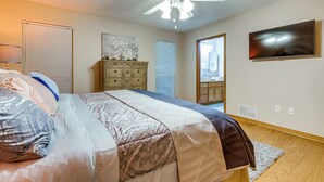 Een slaapkamer met een bed, een plafondventilator, een dressoir en een aan de muur bevestigde televisie.