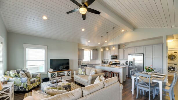 A modern living room with a large sofa, a TV, and a dining area with a table and chairs. - Resort Perks: Waterfront Rockport Home! (Rockport)